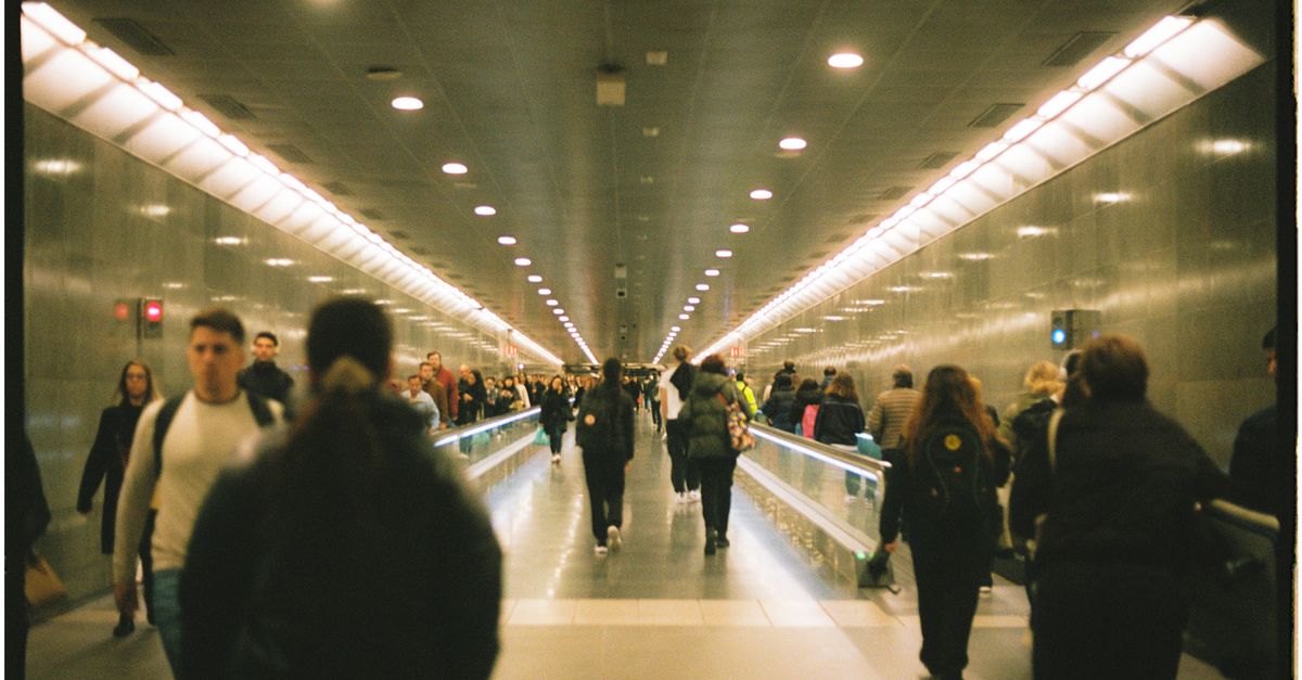 Pasajeros caminando por el pasillo de una terminal de aeropuerto con paneles informativos
